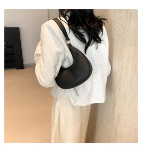 Detail of a black crescent hobo bag with gold metal rings worn on a white tweed jacket