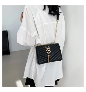 Detail of black V-quilted chain bag with gold metal logo and tassel on a female model