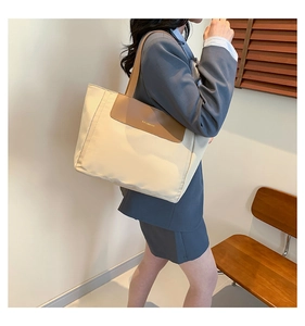 Detail of a beige canvas tote bag with brown leather trim and golden fashion logo on a model