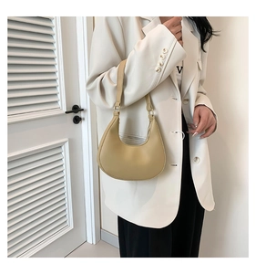 Close-up of beige crescent shoulder bag worn with a white blazer for a chic look
