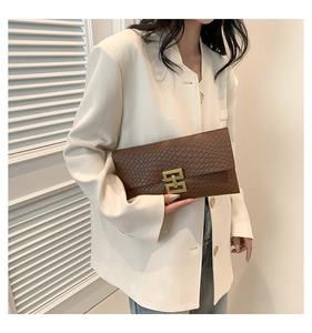 Pochette a busta marrone intrecciata con fibbia dorata abbinata a un blazer bianco