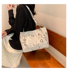 Close-up of white tote bag with letter print and metal chain strap on wooden bench