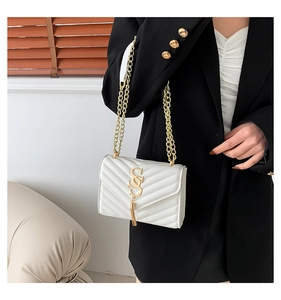 Detail of white chevron quilted leather crossbody bag with gold chain and tassel charm