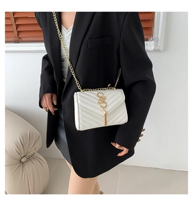 Detail of white V-quilted shoulder bag with gold chain and metal tassel on a model