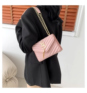 Detail view of pink quilted crossbody bag with gold tassel and SS logo on black blazer