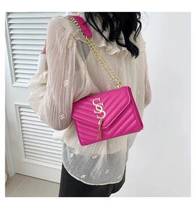Close-up of fuchsia quilted crossbody bag with gold SS logo and elegant tassel detail