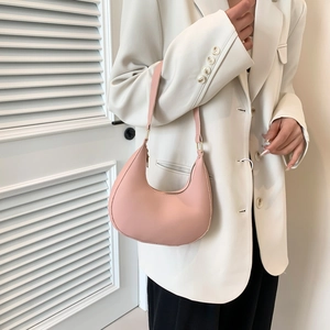 Pink minimalist crescent shoulder bag in matte faux leather worn by a model in a white suit