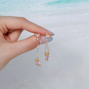 Goldene Bären-Ohrhänger mit rosa Herz und Zirkonia vor einem sommerlichen Strandhintergrund