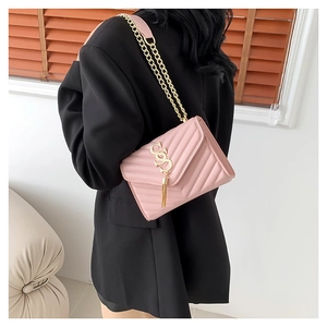 Sac bandoulière matelassé rose avec chaîne dorée et pompon, porté sur un blazer noir