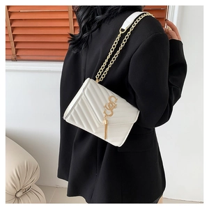Sac bandoulière blanc matelassé en V avec pompon doré sur une veste de blazer noire