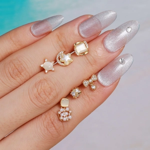 Details van zes gouden oorbellen met parels en stermotieven op handmodel