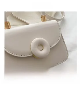 Detailed close-up of cream-white leather handbag featuring a round white decorative buckle