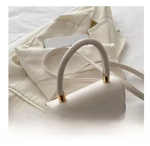 Detailed close-up of cream square handbag with gold cylindrical metal handle and smooth leather