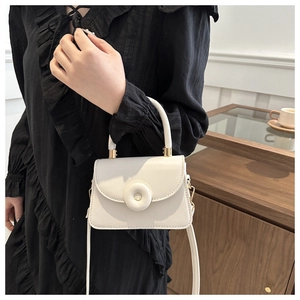 Close-up of white mini square bag featuring round buckle and gold handle connectors