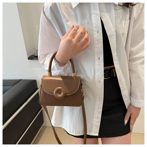 Close-up of a dark brown crossbody bag with round buckle and golden hardware details