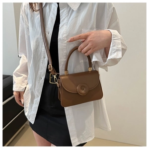 Detail of a brown PU leather crossbody bag with a large circular buckle and gold hardware