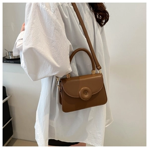 Detail of dark brown leather square crossbody bag with unique round buckle on a model