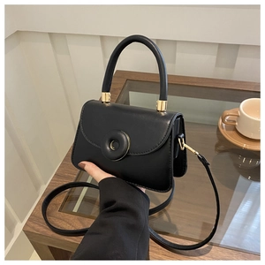 Close-up of black square handbag with golden hardware and leather strap in hand