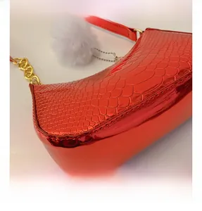 Detail of red croc-embossed patent leather bag with gold chain and white pompom