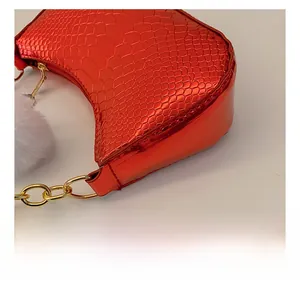 Detail of red croc-embossed leather underarm bag with gold chain and white pompom charm
