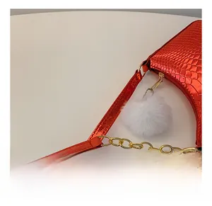 Close-up of red crocodile embossed shoulder bag with gold chain and white fur ball