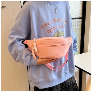 Detail of pink nylon waist bag with woven zipper pull and adjustable strap shown on model