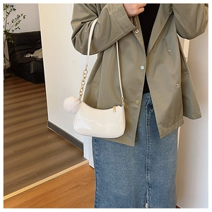 White crocodile embossed baguette bag with gold chain and plush charm on female model