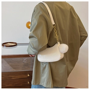 Close-up of white crocodile pattern shoulder bag with gold chain and plush ball detail