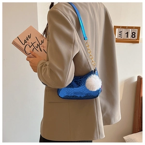 Detail of blue faux snake skin shoulder bag with gold chain and white fur pompom charm