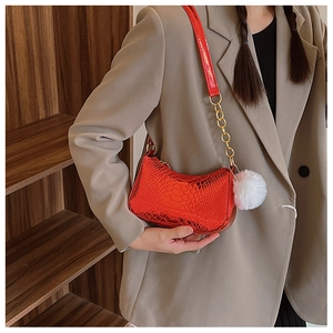 Macro detail of red faux snakeskin texture and gold chain on the crescent armpit bag