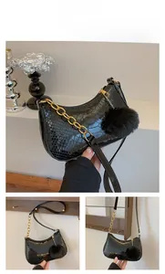 Detail view of black crocodile pattern faux leather handbag with golden chain and fur ball