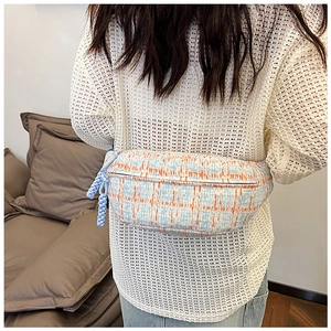 Detail of plaid tweed chest bag in light blue and orange worn as a crossbody bag