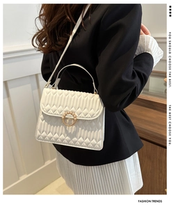 Detail of white quilted crossbody bag featuring a golden circular pearl buckle clasp
