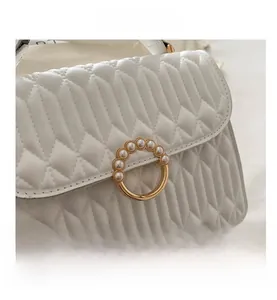 Detailed close-up of white pleated leather handbag with pearl-encrusted gold ring buckle