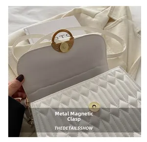 Detail of white quilted handbag showing a golden magnetic snap and smooth PU leather