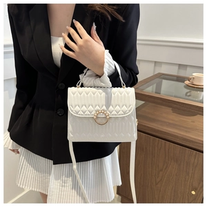 Detail of white quilted crossbody bag with pearl gold buckle worn by a model
