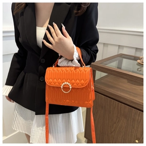 Detail of quilted orange crossbody bag featuring a luxury pearl-embellished metal clasp