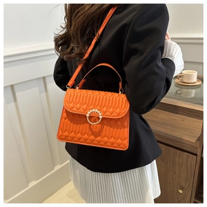 Orange quilted crossbody bag with pearl buckle shown on model in a stylish setting