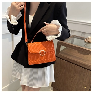 Close-up of orange quilted crossbody bag with pearl ring buckle held by model