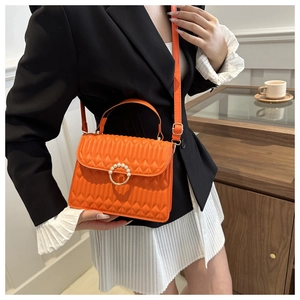 Detail of orange quilted handbag with gold pearl buckle and elegant vertical stitching