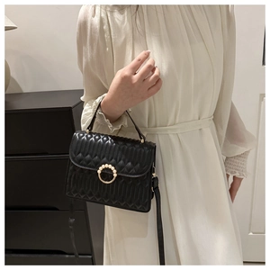 Detail of black quilted leather shoulder bag featuring a pearl gold ring buckle on model
