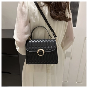 Detail of black quilted shoulder bag with elegant pearl clasp and golden hardware