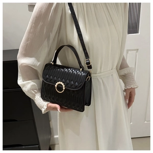 Quilted black crossbody bag with pearl buckle shown on model in white dress