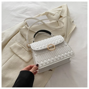 Detail of white quilted crossbody bag featuring a gold clasp with pearl embellishment
