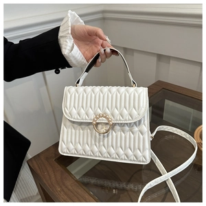 White quilted crossbody bag with pearl buckle shown being held by a model