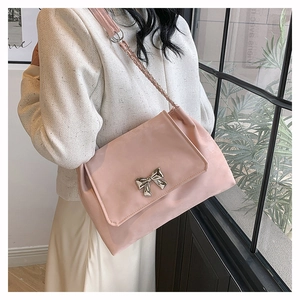 Detail of light pink shoulder bag featuring a silver bow buckle and woven strap design
