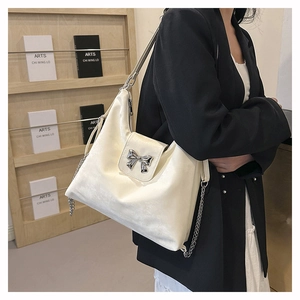 Detail of cream PU leather bag featuring a silver metal bow buckle and chain strap