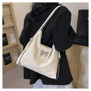 Detailed close-up of a cream-colored hobo bag with a silver metal bow and chain strap