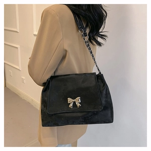 Back view of model wearing a large black PU shoulder bag with silver bow and chain strap