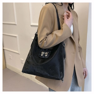 Detail of black PU leather tote with silver bow accent on model in cream blazer